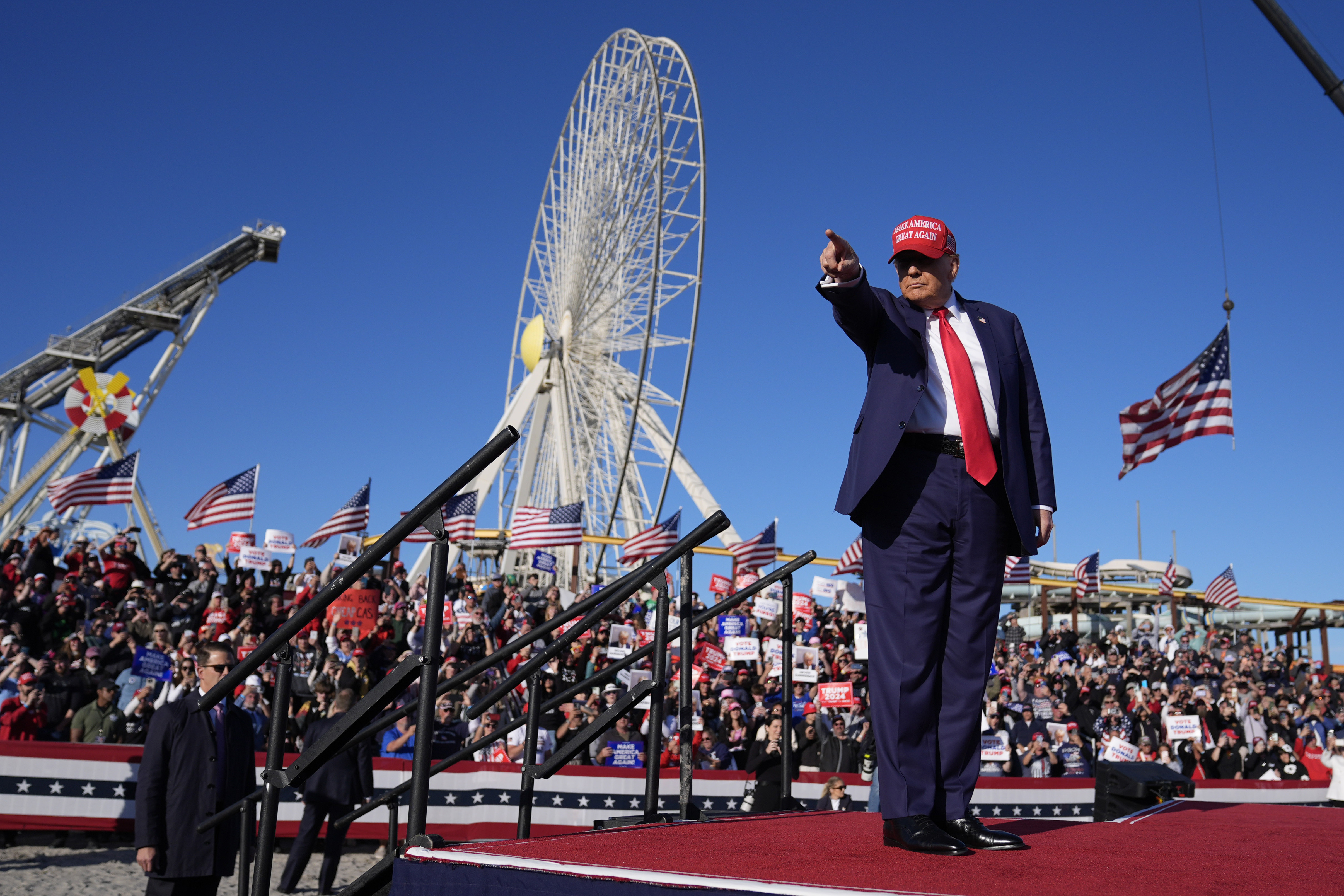 Donald Trump points on stage at a rally as a crowd cheers behind him.